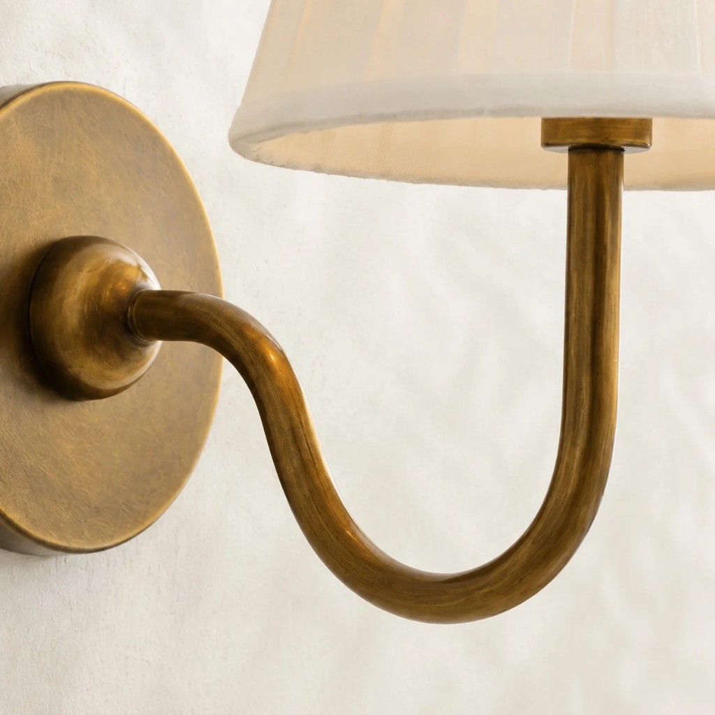 Detailopname van de gebogen messing arm en de geplooide lampenkap.